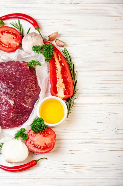 Carne crua com ervas, especiarias e temperos em fundo de madeira branca, ingredientes para cozinhar. Carne de bovino com legumes para sopa ou bife — Fotografia de Stock