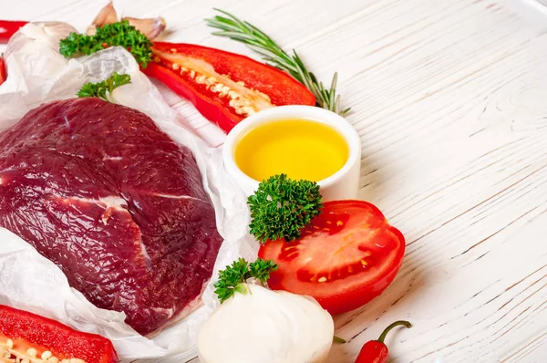 Carne de res con hierbas y especias. Preparación de filetes de carne cruda con aceite, romero, ajo y sazón fresco sobre papel blanco, cerrar — Foto de Stock