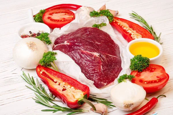 Carne de res con hierbas y especias. Preparación de filetes de carne cruda con aceite, romero, ajo y sazón fresco sobre papel blanco —  Fotos de Stock