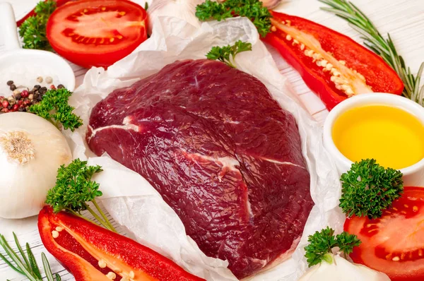 Carne de vaca com ervas e especiarias. Preparação de filé de carne crua com óleo, alecrim, alho e tempero fresco em papel branco — Fotografia de Stock