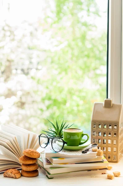 Tazza di caffè, libro aperto, bicchieri, biscotti e fiori sulla finestra con bokeh. Lettura e colazione. Accogliente arredamento domestico — Foto Stock