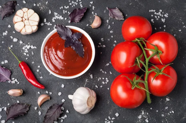 Molho de ketchup de tomate em uma tigela com manjericão, especiarias e tomates na mesa escura — Fotografia de Stock