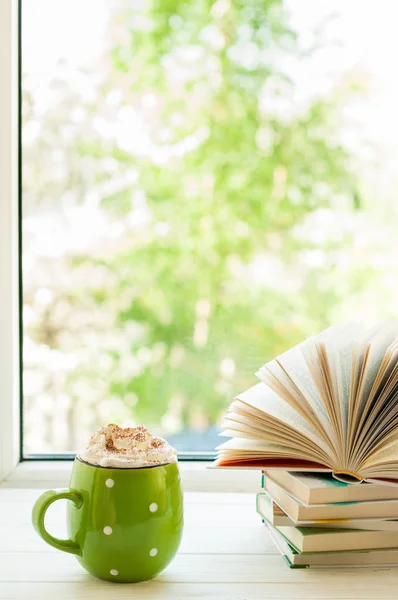Xícara de café com creme e marshmallows, livro aberto na janela com bokeh. Leitura e pequeno almoço — Fotografia de Stock