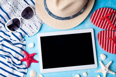 Bayan aksesuarlar yaz: güneş gözlüğü, şapka, flip flop, gömlek ve tablet üzerinde mavi arka plan. Plaj, tatil, seyahat ve serbest