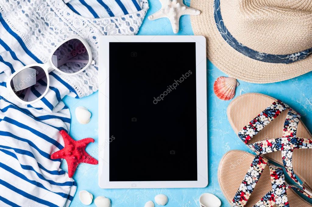 Summer women's accessories: sunglasses, hat, sandals, shirt and tablet on blue background. Vacations, travel and freelance work concept