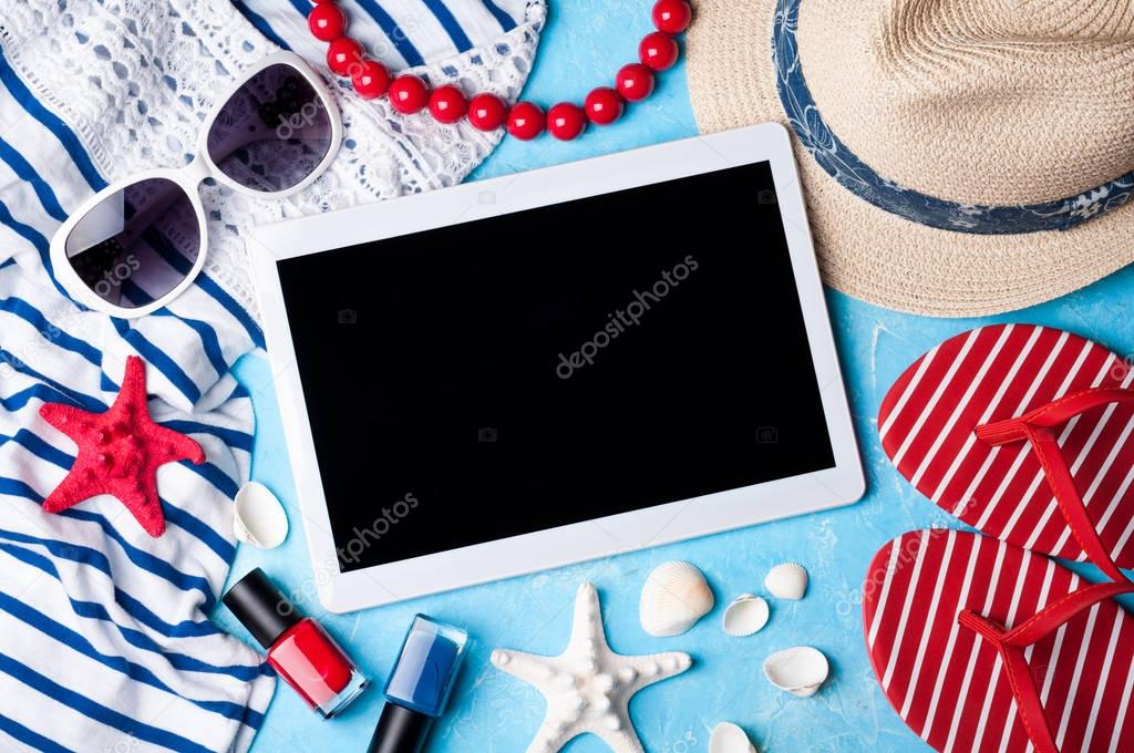Summer women's accessories: sunglasses, hat, flip flop, jewelry, shirt and tablet on blue background. Beach, vacations, travel and freelance