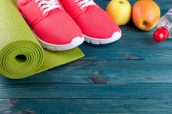 Sport achtergrond. Yoga mat, sportschoenen, water, appels vruchten op houten achtergrond. Gezonde levensstijl, voeding, yoga, sport concept — Stockfoto
