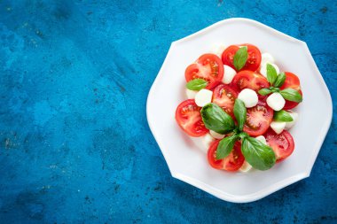 Caprese salatası. Mozzarella peyniri, domates, fesleğen bitki yaprakları mavi beton zemin üzerine. Italyan Mutfagi