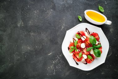 Caprese salatası. Mozzarella peyniri, domates, zeytin yağı, fesleğen bitki yaprakları koyu arka plan üzerinde. Italyan Mutfagi