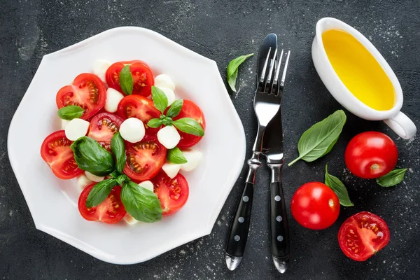 Caprese salatası. Mozzarella peyniri, domates, zeytin yağı, fesleğen bitki yaprakları ve çatal bıçak takımı beton masada. Italyan Mutfagi
