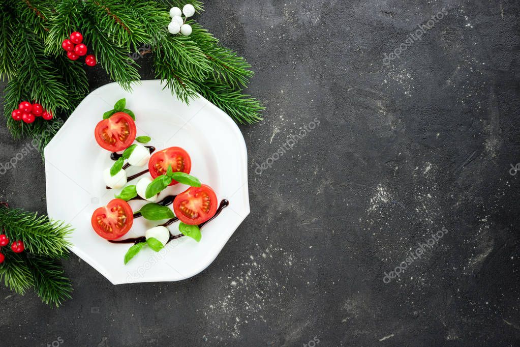 Caprese salad in the shape of Christmas tree. Festive snack on dark background. Christmas table setting concept with salad dish