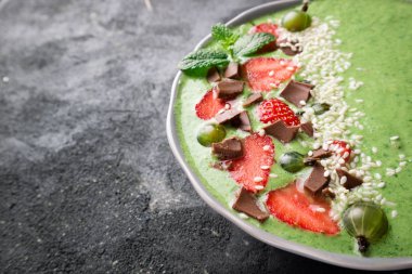 Koyu arka plan üzerinde meyve, berry, çikolata ve susam tohumu ile güler yüzlü kase. Yeşil smoothie kahvaltı için. Süper yiyecek konsepti