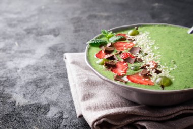 Koyu arka plan üzerinde meyve, berry, çikolata ve susam tohumu ile güler yüzlü kase. Sağlıklı kahvaltı için yeşil smoothie