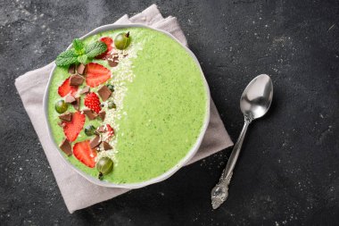 Karanlık beton zemin üzerine meyve, berry, çikolata ve susam tohumu ile güler yüzlü kase. Yeşil smoothie üstten görünüm. Sağlıklı yemek, Kahvaltı ve diyet