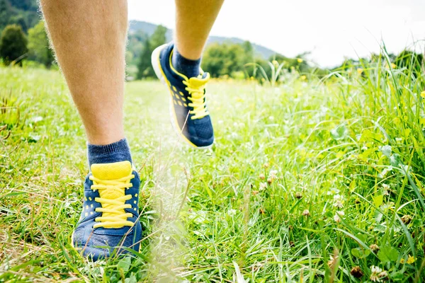 Young fitness man runner athlete running at green grass in park. Runner feet running. Sport background concept