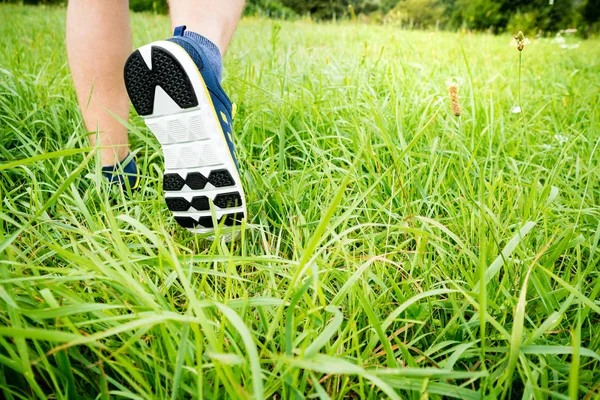 Fitness man runner athlete running at green grass in park. Men\'s legs running closeup. Sport hiking tourism