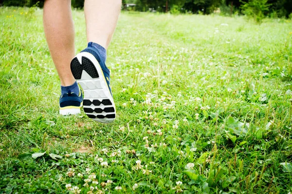 Спортсмен фітнесу біжить на зеленій траві в парку. Чоловічі ноги бігають крупним планом. Спорт пішохідний туризм — стокове фото