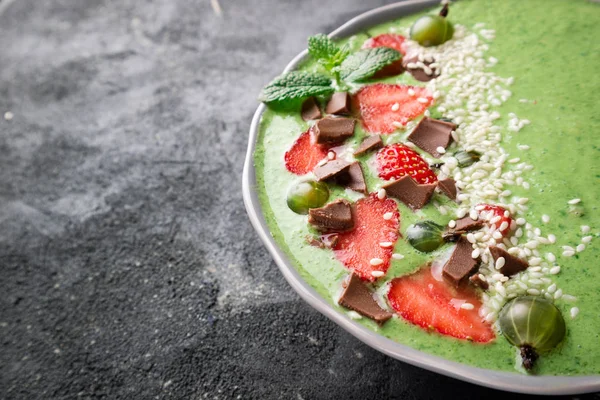Smoothie bowl with fruits, berry, chocolate and sesame seeds on dark background. Green smoothie for breakfast. Super food concept