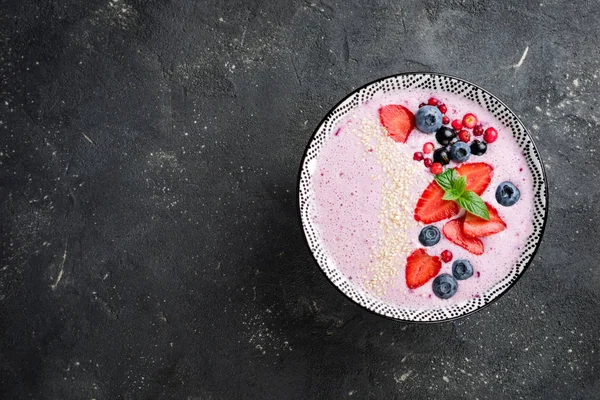 스무디는 딸기, 딸기, 블루베리, 크랜베리, 건포도와 그릇. 어두운 배경에 핑크 스무디 건강 식품 및 다이어트 개념입니다. 상위 뷰 — 스톡 사진