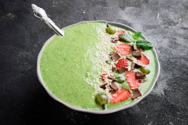 Karanlık beton zemin üzerine meyve, berry, çikolata ve susam tohumu ile güler yüzlü kase