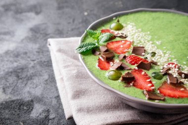 Kivi, ıspanak, çilek, bektaşi üzümü, çikolata ve susam tohumu karanlık beton arka plan üzerinde ile güler yüzlü kase. Sağlıklı yemek, Kahvaltı ve diyet kavramı