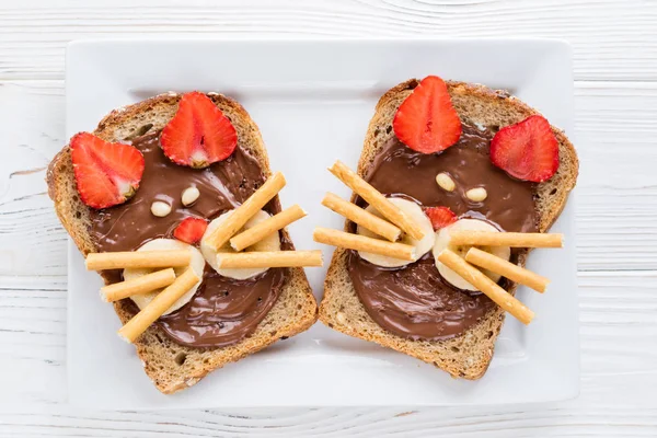 Kinderfrühstück mit Sandwiches und Milch. Lustige Katzen Gesicht Sandwiches mit Beeren, Schokolade, Bananen, Nüssen — Stockfoto