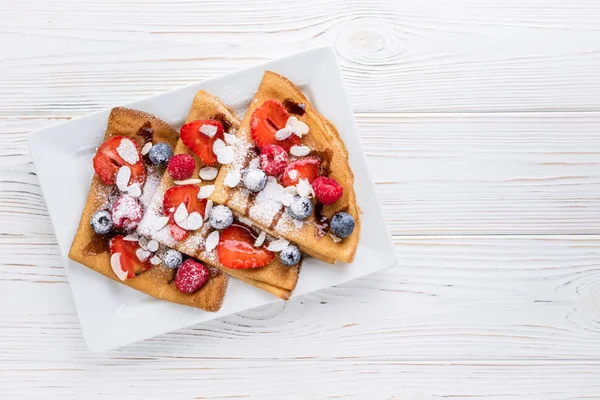 Κρέπες με φράουλες, βατόμουρα, αμύγδαλο και σοκολάτα σάλτσα σε άσπρο φόντο ξύλινη. Το Top view — Φωτογραφία Αρχείου