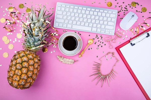 Platt lekmanna fashion feminina hemmakontor arbetsyta. Festlig kvinnans bakgrund. Ananas, kaffekopp, gyllene konfetti och smycken på rosa bord — Stockfoto