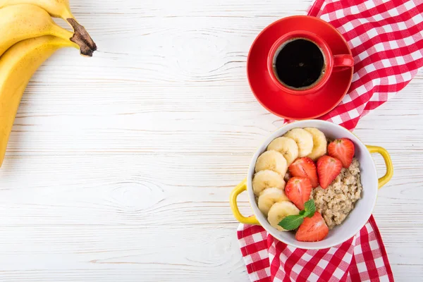 Yulaf lapası, kahve fincanı, meyveler ve meyve kahvaltı. Çilek ve muz yulaf ezmesi. Sağlıklı kahvaltı konsepti