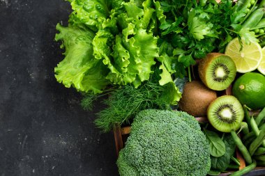 Yeşil sebze. Brokoli, ıspanak, kivi, marul, maydanoz, dereotu, kuşkonmaz fasulye karanlık beton masada. Vejetaryen yiyecekler