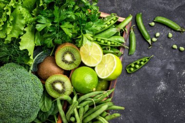 Yeşil sebzeler arka plan. Brokoli, ıspanak, kivi, marul, maydanoz, dereotu, kuşkonmaz fasulye karanlık beton masada. Taze Bahçe üretmek. Üstten Görünüm