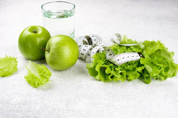 Здоровое питание. Зеленое яблоко, салат из салата, стакан воды, измерительная лента. Диета, похудение, потеря веса и планирование еды — стоковое фото