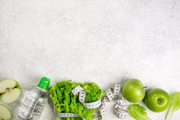 Здоровое питание. Зеленое яблоко, салат из салата, бутылка воды, измерительная лента на белом фоне. Диета, похудение, здоровое питание. Копирование пространства — стоковое фото