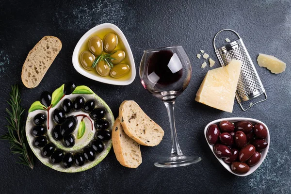 Azeitonas, vinho tinto, pão de ciabatta, queijo, óleo, ervas e especiarias sobre fundo de pedra preta. Lanches mediterrânicos. Appetizer comida gourman — Fotografia de Stock