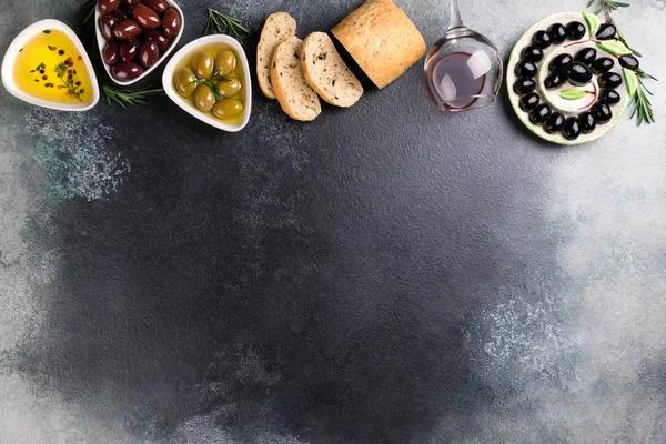 Azeitonas, vinho tinto, pão de ciabatta, óleo, ervas e especiarias sobre fundo de pedra preta. Lanches mediterrânicos. Appetizer comida gourman — Fotografia de Stock