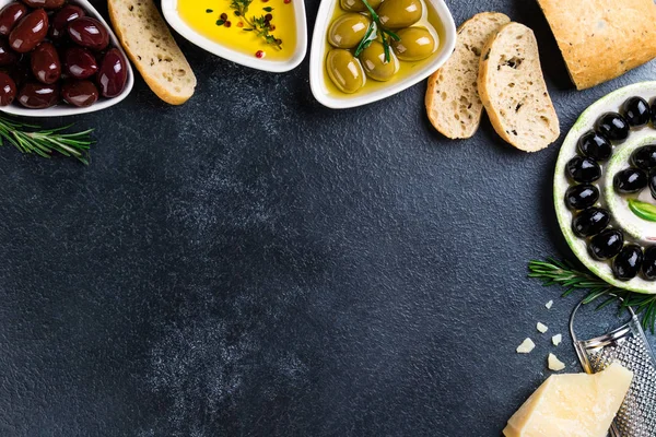 Olives, ciabatta bread, cheese, oil, herbs and spices on black stone background. Mediterranean snacks. Appetizer gourman food. Copy space — Stock Photo, Image