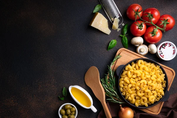 Massa e ingredientes para cozinhar em fundo escuro, vista superior. Conceito de comida italiana. Massas alimentícias, tomates, manjericão, legumes e especiarias — Fotografia de Stock