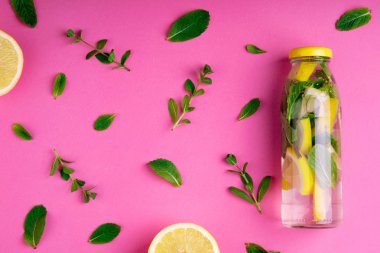 Pembe bir arka plan üzerinde tropikal su şişe. Detoks meyve suyu, narenciye ve nane yaprakları infüzyon