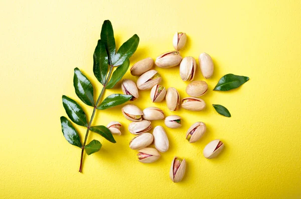Pistachios with leaves on yellow background, top view. Set of pistachio nuts — Stock Photo, Image