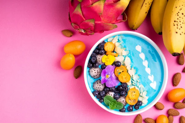 Smoothie bowl with fruits, berries, nuts and flowers. Tropical healthy smoothie dessert. Healthy breakfast, vegetarian, dieting concept