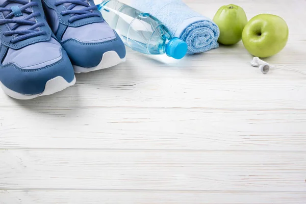 Zapatillas deportivas planas, botella de agua, manzanas, toallas y auriculares sobre fondo de madera blanca. Equipamiento deportivo. Vida sana, deporte y concepto de dieta — Foto de Stock