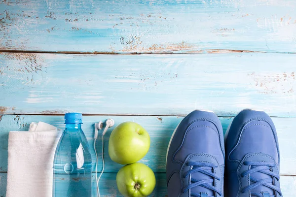 Plochá laických sportovní boty, láhev vody, jablka, ručník a sluchátka na bílém pozadí. Sportovní vybavení — Stock fotografie