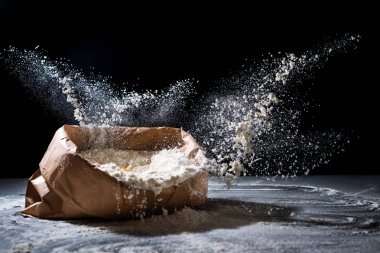 Un ve un içinde siyah arka plan üzerinde uçan yumurta ile çanta. Un sıçrama. Yemek, pişirme kavramı