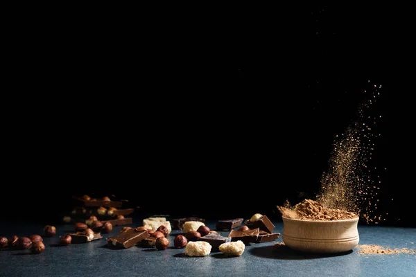 Cocoa powder in motion. Chocolate dust, cacao products, nuts on black background. Copy space