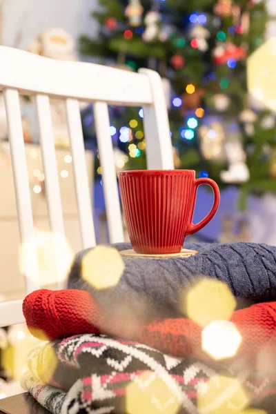 Γιορτινά Χριστούγεννα φόντο με κόκκινο καφέ κούπα ή τσάι, βιβλία, ζεστά πουλόβερ. Χριστουγεννιάτικο δέντρο με φώτα bokeh. Διακοπές, Χριστούγεννα, γιορτινή, άνετο σπίτι, ξεκούραση — Φωτογραφία Αρχείου