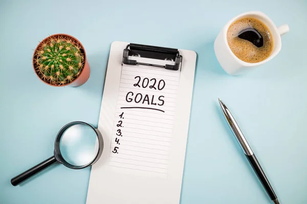 Top view 2020 goals list with notebook and coffee cup on blue desk. 2020 resolutions, goal, plan, strategy, change, idea