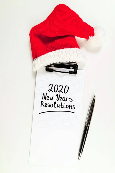 Resoluciones de año nuevo 2020 sobre el escritorio. Lista de goles 2020 con cuaderno, sombrero de santa y bolígrafo sobre fondo blanco. Objetivo, plan, estrategia, cambio, concepto de idea —  Fotos de Stock