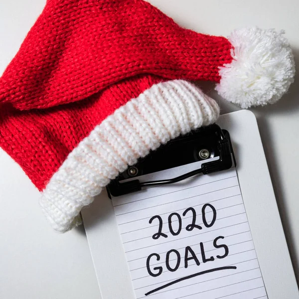 机の上の新年の目標2020 。白を背景にノートと赤のサンタの帽子と2020年の目標 — ストック写真