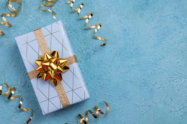 Holidays gift box wrapped in blue geometric paper on blue background. Happy Holidays, Christmas, Happy birthday concept