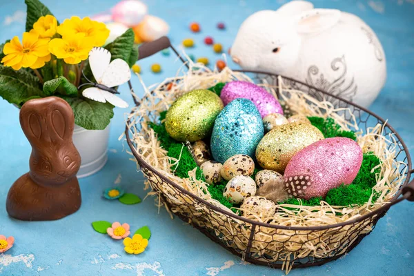 Spring Easter background for holiday. Easter composition with colorful Easter eggs on moss in basket, bunny and spring flower pot. Top view